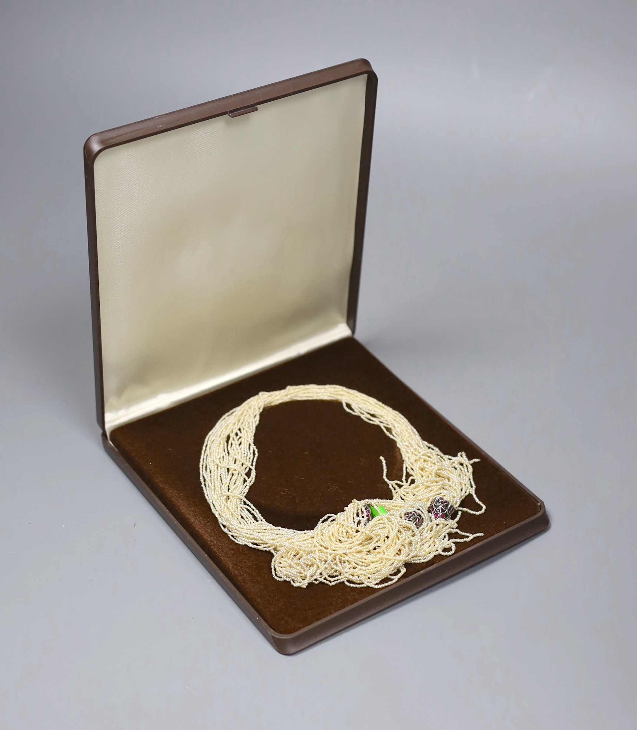 An Indian multi-strand seed pearl sautoir necklace, with ruby set white metal terminals, length 130cm
